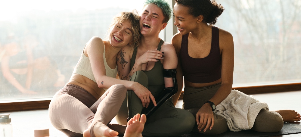 Group of happy young girls laughing together sitting on yoga mats after class