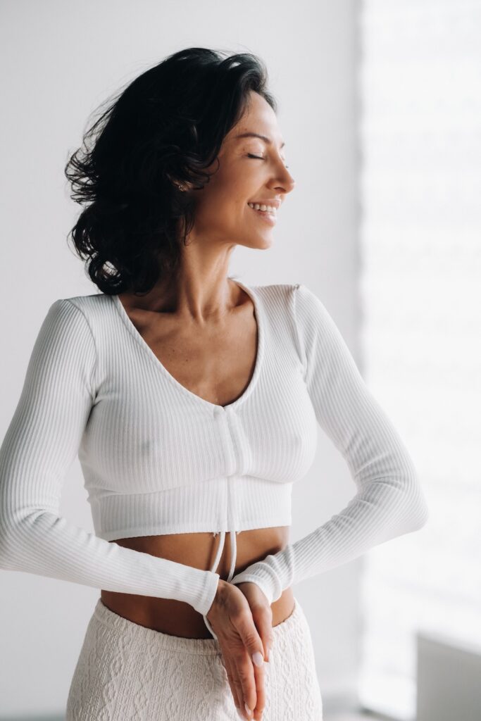 Female in white clothes stands with her hands clasped at the bottom