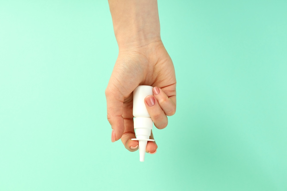 Female hand holds blank bottle of nasal spray on mint background