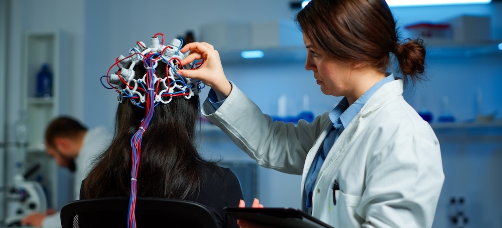 Woman patient wearing performant eeg headset scanning brain electrical activity in neurological research laboratory while medical researcher adjusting it