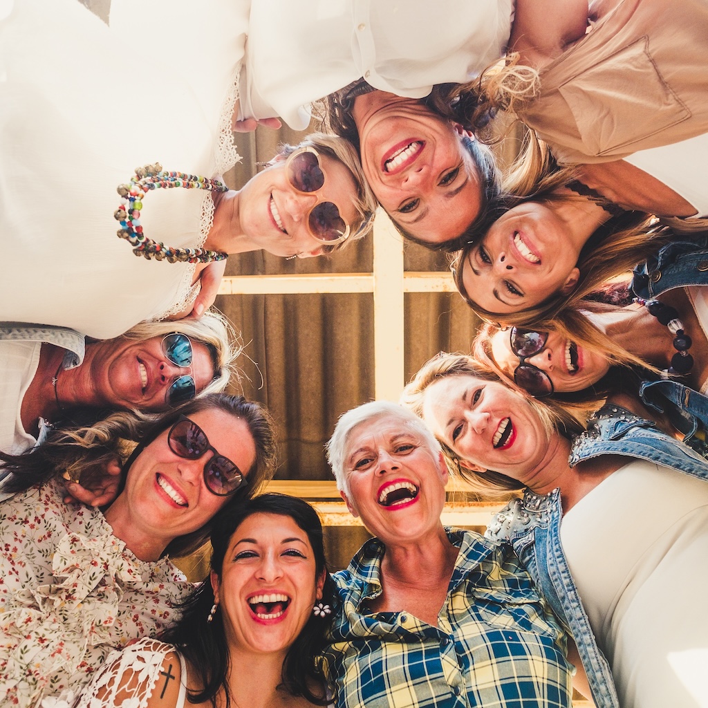 Happy, laughing group of women in friendship enjoying their time together in outpatient treatment, looking down at the camera.