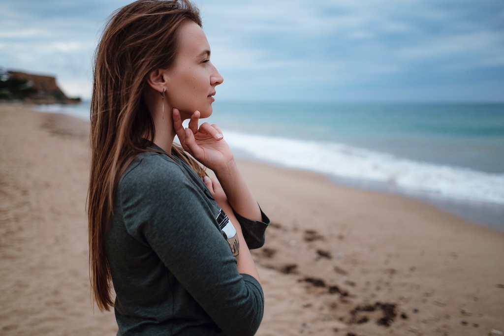 Young adult woman thoughtfully gazing in to the distance on the beach in the winter.