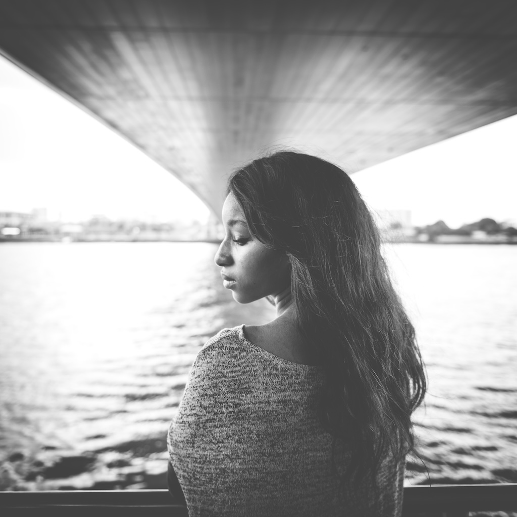 Depressed young woman looking down at the ground near the water.