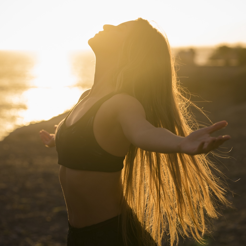 Young healthy woman enjoying the sunset while opening arms