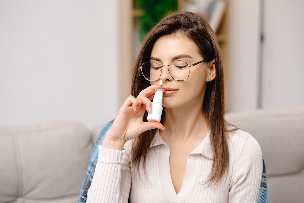 Young woman wearing casual clothing, using a nasal spray, Spravato