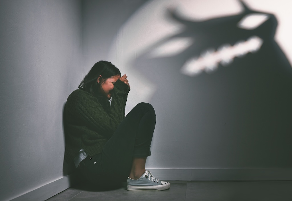 Shot of a young woman sitting in the corner of a dark room struggling with treatment resistant depression.